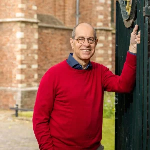 Glimlachende man in rode trui bij een monumentale toegangspoort
