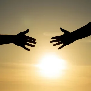 Twee silhouetten van reikende handen tegen een gouden zonsondergang